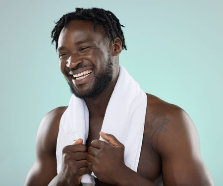 Face, skin and beauty of a man in studio with towel for hygiene and grooming. Healthy and happy black person on blue background for facial glow, cosmetics and self care with skincare dermatologyの写真素材