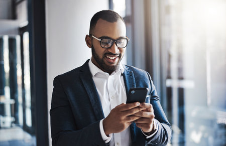 All updates get sent straight to him. a young businessman using a cellphone in an office.の写真素材