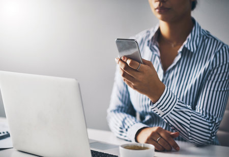 She has tasks set on all her devices. Closeup shot of an unrecognizable businesswoman using a cellphone in an office.の写真素材
