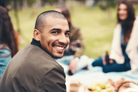 Happy to be here with my close friends. Portrait of a cheerful young man seated with his friends at a picnic outside during the day.の写真素材