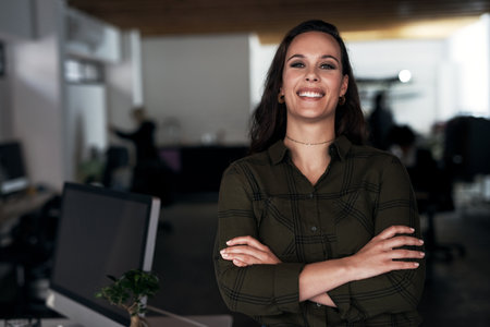 This is what a successful smile looks like. an attractive young businesswoman standing alone with her arms crossed in the office.の写真素材