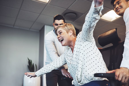 Shes soaring in the office. businesspeople having fun by taking their colleague for a ride in her chair in the office.の写真素材