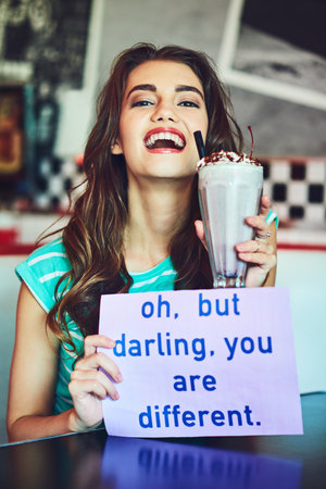 Stand out. an attractive young woman holding up a sign while enjoying a milkshake in a retro diner.の写真素材