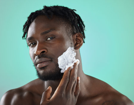 Black man, apply foam and studio portrait for shaving, skincare or safety for cosmetics by blue background. African gen z model, hair removal cream of face beauty for aesthetic, cleaning or self careの写真素材