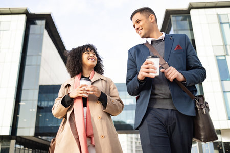Conversation, coffee break and happy business people walking, talking or travel in urban New York. Architecture, black woman or employee partnership team on morning commute journey to office buildingの写真素材