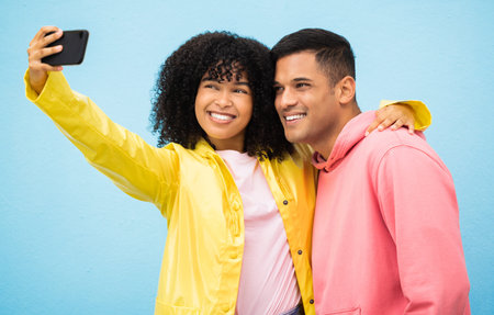 Happy couple, bonding and phone selfie on isolated blue background for social media, profile picture and travel vlog. Smile, happy man and black woman on mobile photography technology in Brazil cityの写真素材