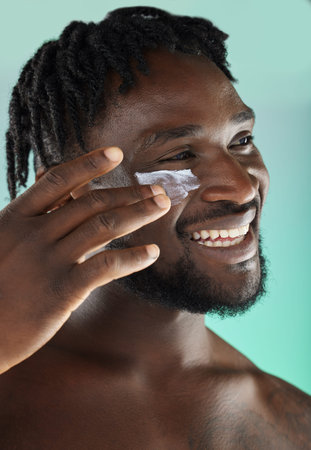 Black man, face and cream with smile and beauty, moisturizer for skincare isolated on studio...
