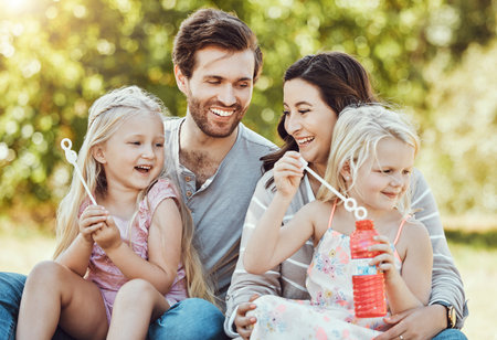 Family, bubbles and park fun outdoor feeling happiness, love and parent care with children. Happy mom, dad and girl kids in nature on grass relax on vacation on summer holiday together with a smileの写真素材
