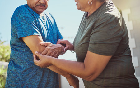 Senior, man arm injury and woman helping husband after exercise, fitness and workout accident. Elderly, arthritis and joint pain with a couple in retirement outdoor for health and wellness activityの写真素材