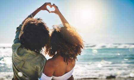We would be incomplete without each other. Rearview shot of two friends forming a heart shape together on the beach.の写真素材