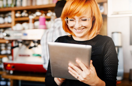 The customers really gave some great reviews. a young woman using a digital tablet while working in a coffee shop.の写真素材