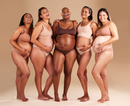 Pregnancy, body and portrait of happy friends in a studio for diversity, motherhood and prenatal wellness. Maternity, beauty and pregnant women showing baby bump stomach together by beige background.の写真素材