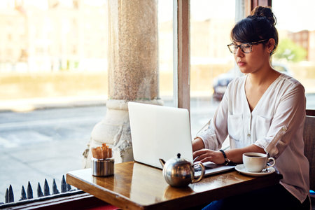 Lets get cracking. a beautiful young woman using a laptop in a cafe.の写真素材