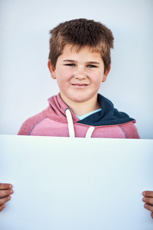 I really like this idea. Portrait of a little boy holding a blank board against a grey background.の写真素材