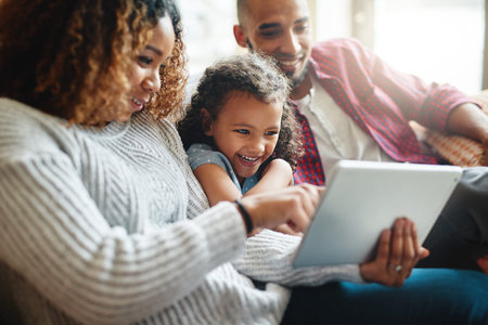 I wanna play this game mommy. an adorable little girl using a digital tablet with her parents in...