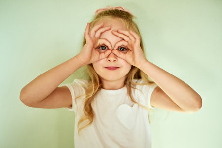Ive got glasses on. Portrait of a cheerful little girl making a face with her hands while looking into the camera at home.の写真素材