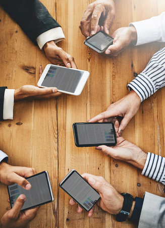 You wont have to carry hardcopies ever again. a group of unrecognisable businesspeople using their cellphones in synchronicity.の写真素材