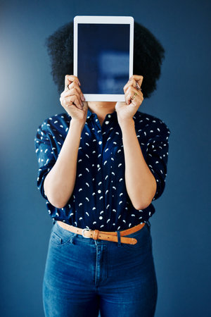 Lets get your app visible. Cropped studio shot of a young woman covering her face with a blank digital tablet against a blue background.の写真素材