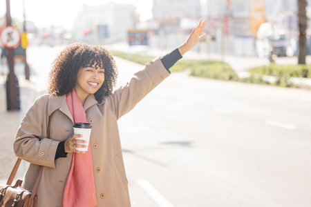 Taxi, coffee and commuting with a business black woman calling or hailing a cab outdoor in the city. Street, travel and transport with a female using ride share to commute in an urban townの写真素材