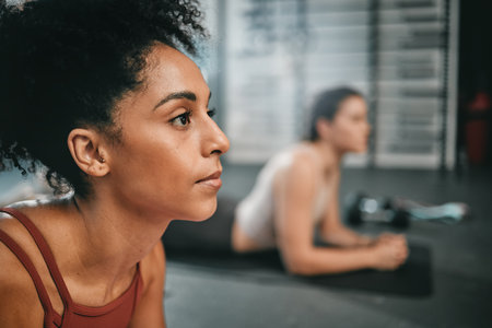 Black woman, gym focus and plank exercise of a person on the floor busy with workout and wellness. Sports, ground training and strength performance challenge of girl friends at a fitness health clubの写真素材