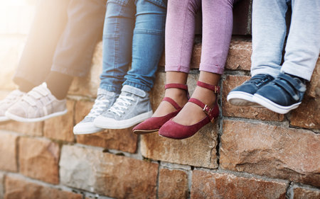 New shoes for the new school year. unrecognizable elementary school kids sitting on a brick wall outside.の写真素材