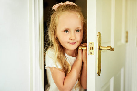 Okay you found me. Portrait of a cheerful little girl opening a door while looking into the camera at home.の写真素材