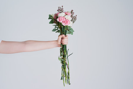Because everyone deserves flowers. Studio shot of an unrecognizable woman holding a bunch of flowers against a grey background.の写真素材