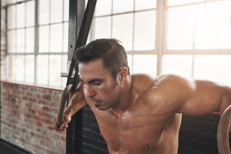 Get up and make those muscles. a muscular young man exercising with gymnastic rings in a gym.