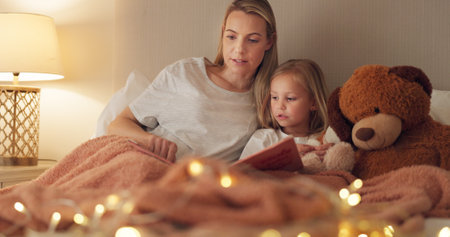 Story, book and reading mother with child in bedroom for child education, home learning or language development together. Mom and girl kid with creative literature for kindergarten with lamp lightsの写真素材