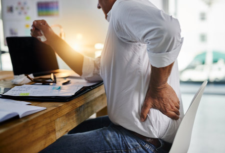Sitting all day has brought this pain. a mature businessman experiencing body discomfort at work.の写真素材