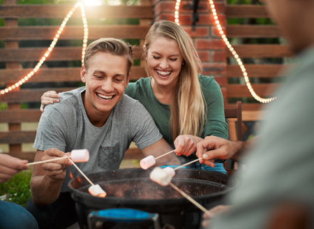 I havent done this in a while. a group cheerful young friends holding up marshmallows on sticks over a fire outside.の写真素材