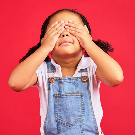 Little girl, hands and eyes cover on isolated red background for shy, mistake expression and...