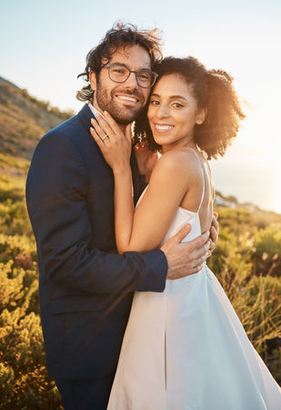 Portrait, interracial and bride with groom for wedding at sunset in nature, hug and celebrate love and relationship. Face, couple and marriage by black woman and man smile, hug and happyの写真素材