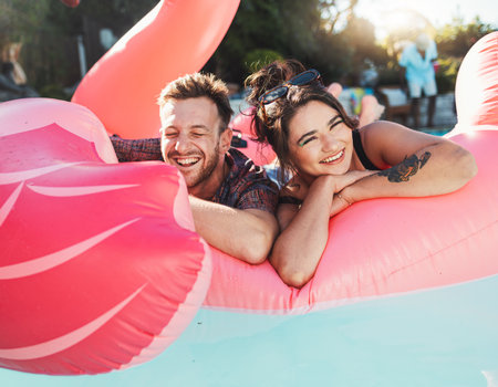 Pool party, portrait and happy couple floating in the water together while on vacation at a resort. Float, summer and young man and woman in a swimming pool having fun on a holiday or weekend trip.の写真素材