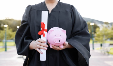 Piggy bank, saving and university diploma in hands of woman graduate with education scroll. Study paper, scholarship and college trust fund of a woman hand at college event with money for futureの写真素材