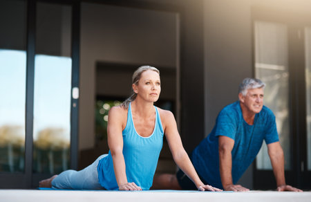 Starting off our day with a much needed yoga session. Full length shot of a mature and happy couple doing yoga exercises outside of their home.の写真素材