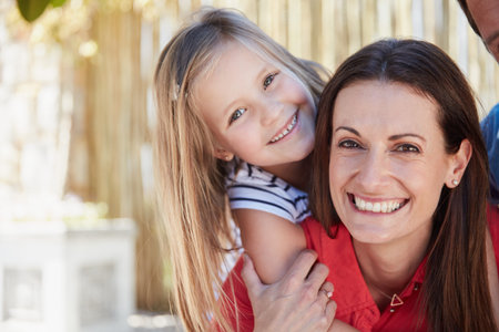 Enjoying a day with mom. Portrait of smiling mother giving her young daughter a piggyback outside in...