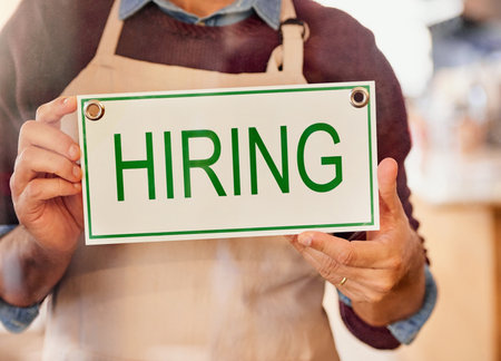Looking for some good help. an unidentifiable business owner holding up a sign that reads hiring in his shop window.の写真素材