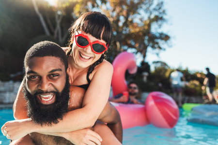 Love, pool party and couple piggyback, having fun and bonding. Swimming, romance diversity and portrait of happy man carrying woman in water and laughing at funny joke at summer event or celebration.の写真素材