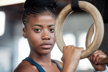 Fitness, gymnastics and portrait of a black woman with rings for training, muscle and arms at gym. Focus, strong and face of an African gymnast with performance during a workout or exercise at a clubの写真素材