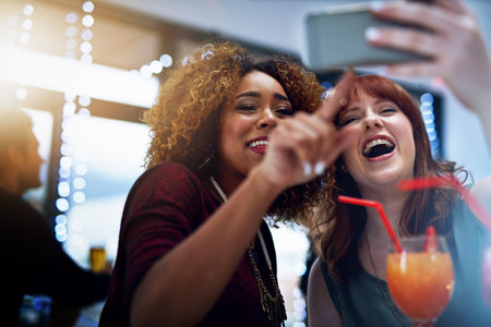 We look so funny in that one. two young friends taking a selfie while having drinks at a party.