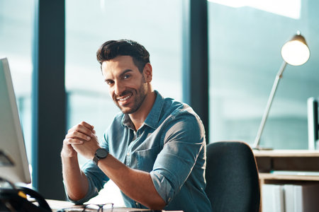 Its hard not to smile making a success of business. Portrait of a young businessman working at his desk in a modern office.の写真素材