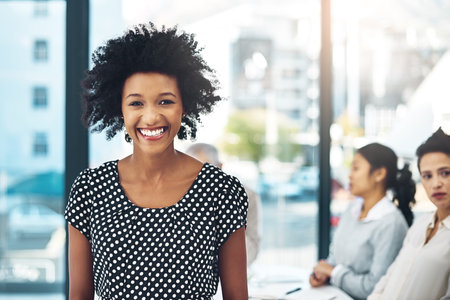 I feel honoured to work with such an amazing team. Portrait of a young businesswoman standing in an office with her colleagues in the background.の写真素材
