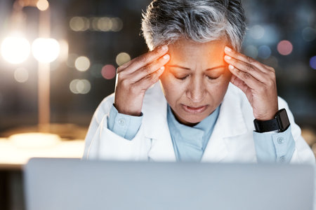 Night, stress and headache with doctor at laptop for medical, stress and deadline review. Burnout,...