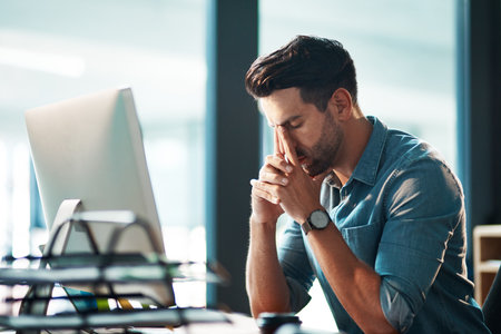 It might be time to call it a day. a young businessman experiencing stress while using a computer in a modern office.の写真素材