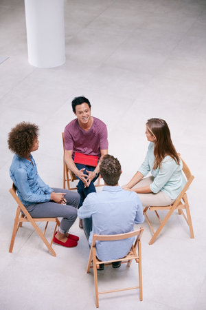Gathering for new ideas. High angle shot of a group of businesspeople talking together while sitting in a circle in an office.の写真素材