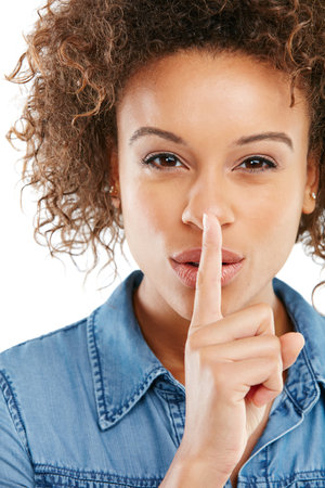 Lets keep it between us. a young woman keeping her finger on her lips against a white background.の写真素材