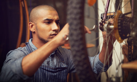 Hes wheely good at what he does. a young man repairing a bicycle wheel in his workshop.