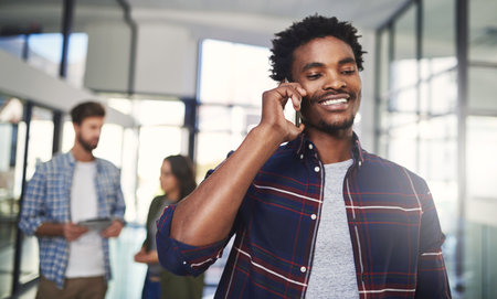 Networking is essential in a modern office. a young designer talking on a cellphone in an office with colleagues in the background.の写真素材