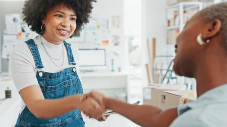 Women, envelope and smile with handshake in deal at studio or business in home. Black woman, entrepreneur or designer get letter, document or paperwork, at office in house and say thank you to clientの写真素材